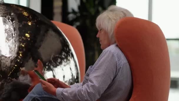 Женщина сидит на мобильном телефоне в удобном кресле — стоковое видео