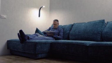 Geceleri rahat bir gündüz yatağında kitap okuyan bir adam.