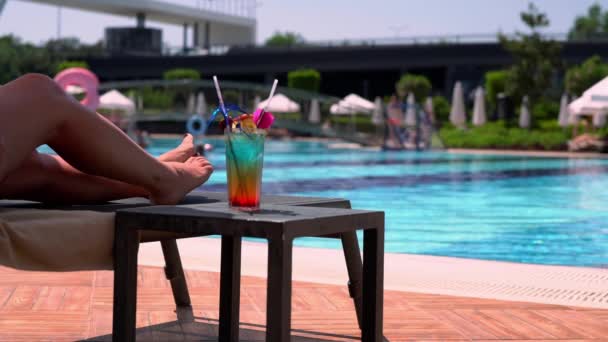 Bain de soleil femme à côté d'une piscine scintillante avec un cocktail — Video