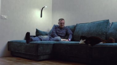 Orta yaşlı bir adam evcil kedisiyle kanepede dinleniyor.