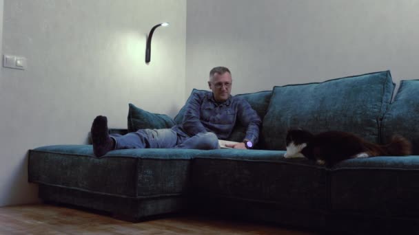 Medelålders man koppla av med sin katt på en soffa — Stockvideo