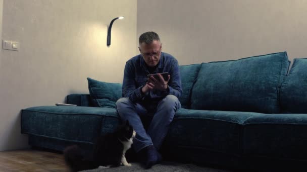 Mann sitzt mit Handy und Katze zu Füßen — Stockvideo