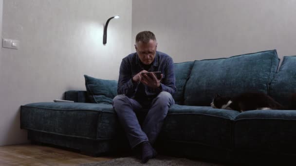 Homem concentrando-se em seu telefone celular assistido por um gato — Vídeo de Stock