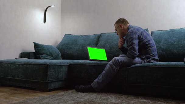 Mand sidder på en stor komfortabel sofa med sin bærbare computer – Stock-video