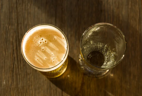 Накладные расходы на бокал пива рядом с пустым стеклом — стоковое фото