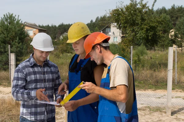 Tres constructores discutiendo el papeleo en un sitio — Foto de Stock