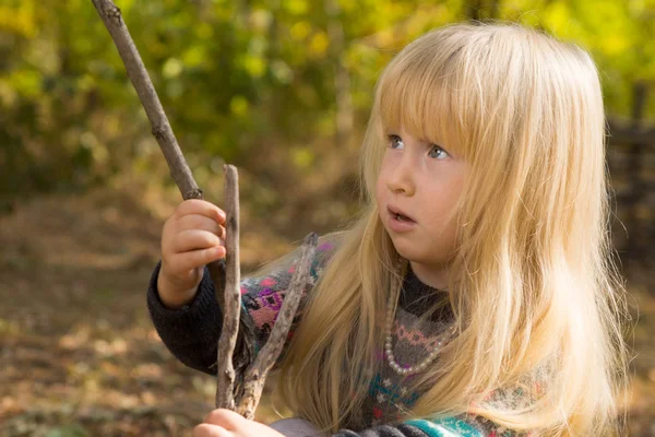 Liten blond flicka leker med en trä filial — Stockfoto