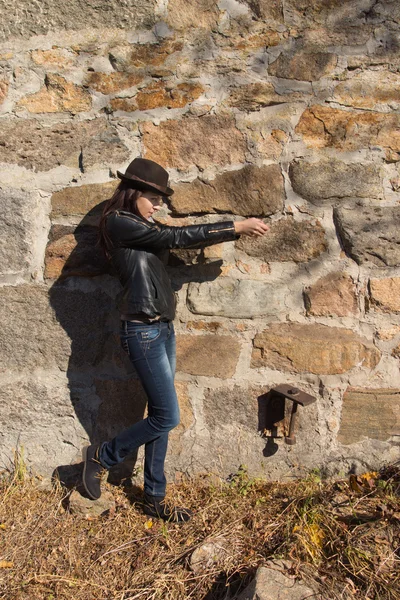 Mulher jovem chique esbelto na frente de uma parede de pedra — Fotografia de Stock