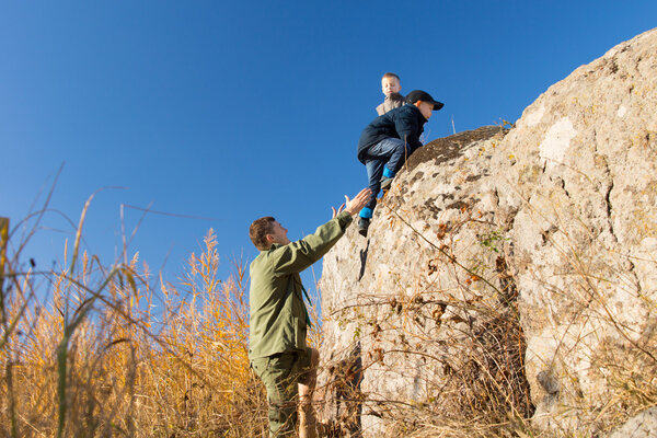 Молодой человек помогает двум мальчикам взобраться на камень
