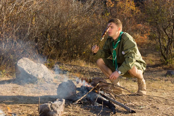 Hungry young scout cooking sausages — Stock Photo, Image