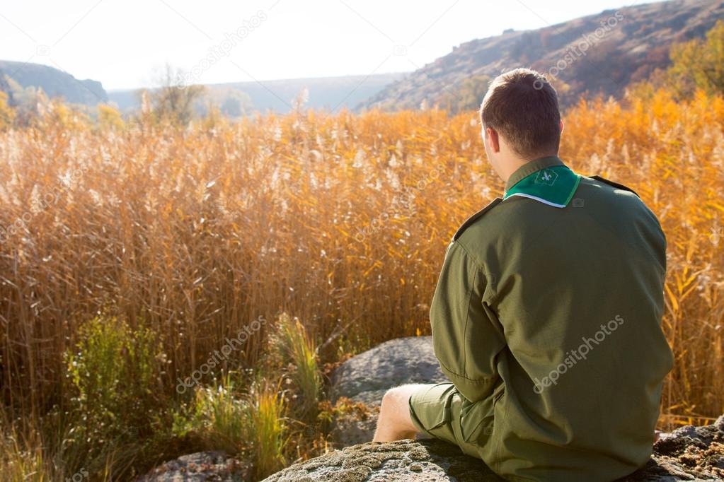 Boy Scout Sitting on the Rock Watching Brown Field