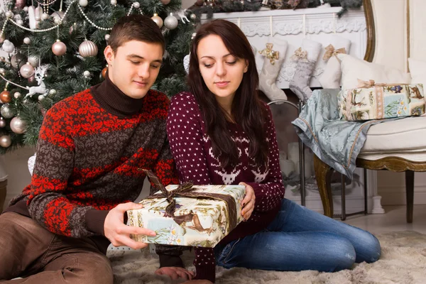 Mladý pár sedí na podlaze drží jeden dárek — Stock fotografie