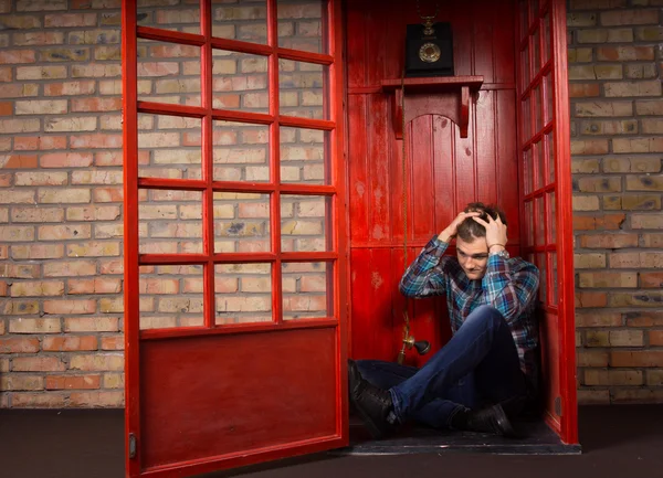 Человек с бедами сидит на полу телефонной будки — стоковое фото