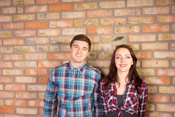 Pareja sonriente de pie frente a la pared de ladrillo —  Fotos de Stock