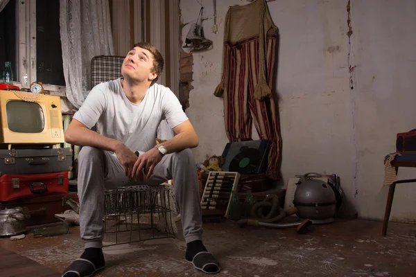 Sitzender junger Mann im verdreckten Zimmer, der nach oben schaut — Stockfoto