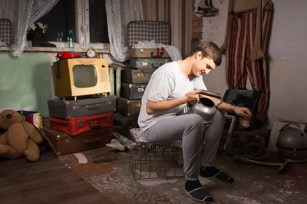 Sitting Man Holding Unused Kettle at Junk Room — Stock Photo, Image