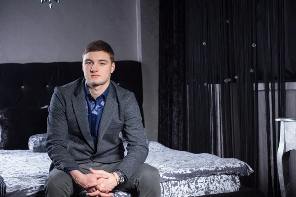 Mladý muž v formální oblečení, sedí na posteli — Stock fotografie