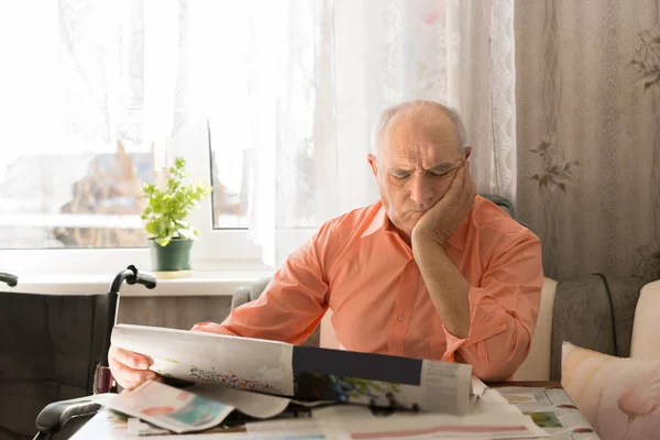 Anciano leyendo periódico con la mano en la cara — Foto de Stock