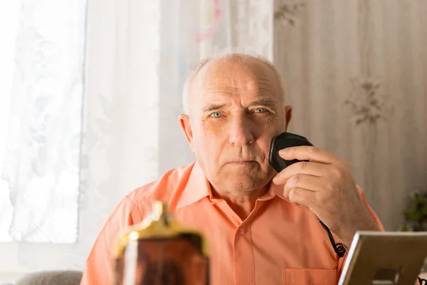 Старик бреет волосы на лице с электрической бритвой — стоковое фото