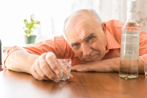 Dronken ouderen houden schot glas aan de tafel — Stockfoto