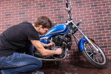 Sitting Young Guy Repairing his Motorcycle clipart