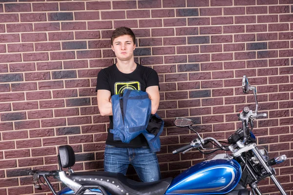 Ung Man står med sin jacka och motorcykel — Stockfoto