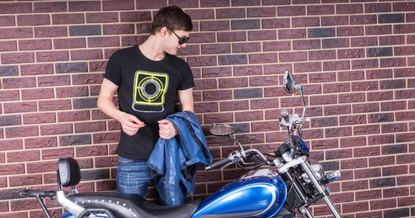 Hombre sosteniendo una chaqueta mirando su motocicleta — Foto de Stock