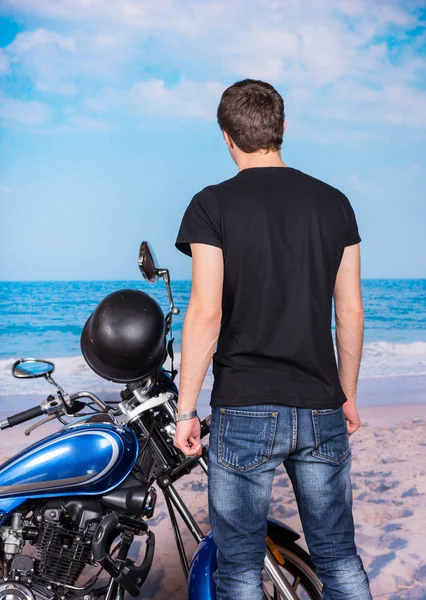 年轻男子站在海滩上的摩托车旁边 — 图库照片
