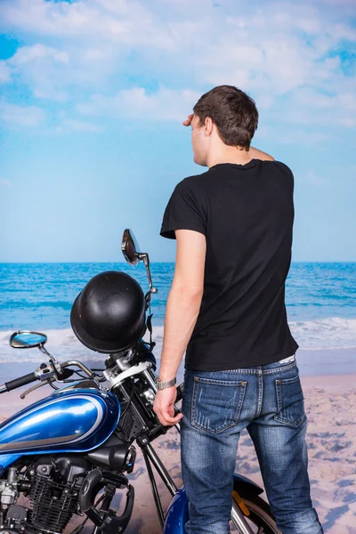 Mand med motorcykel kigger ind i afstand på stranden - Stock-foto