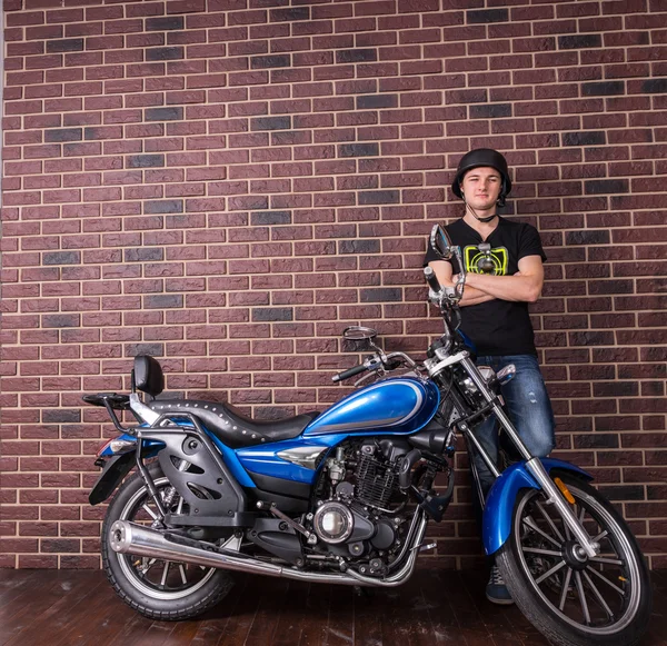 Joven hombre parado al lado de la motocicleta contra la pared — Foto de Stock