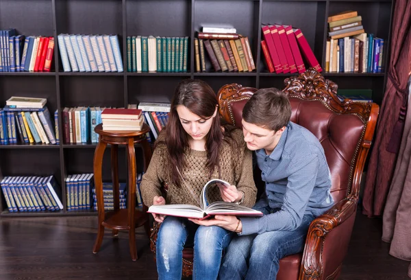 Ernstes junges Paar auf einem Stuhl beim Lesen eines Buches — Stockfoto