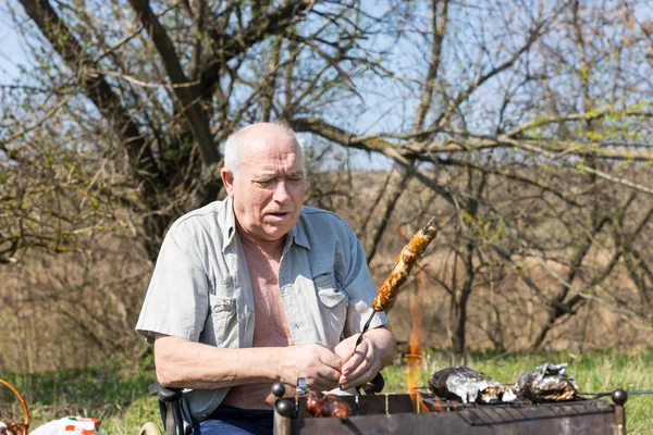 Homme âgé assis rôtissant de la viande au terrain de camping — Photo