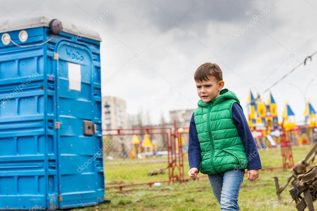 Boy passing near a blue portable toilet in a park