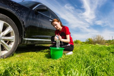 Woman Washing Black Car in Field with Soapy Sponge clipart