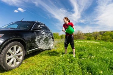 Woman Washing Car with Bucket of Water in Field clipart