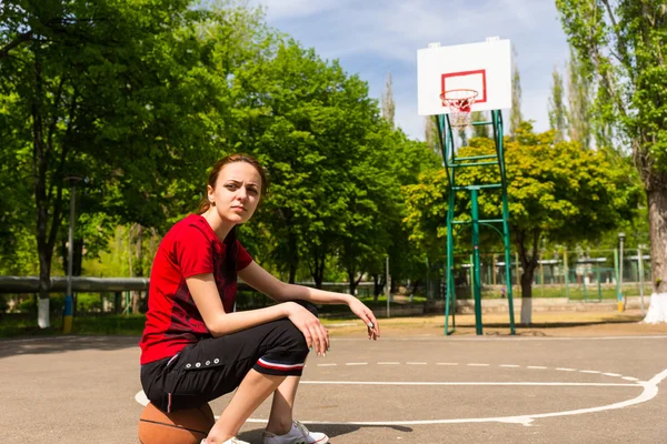 Athletic Woman Sitting on Basketball on Court — Stock Photo, Image