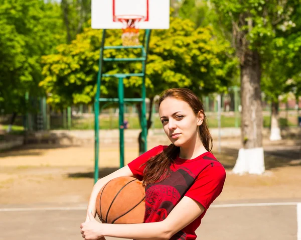 Perempuan berdiri di lapangan basket memegang bola — Stok Foto