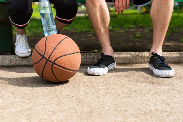 Basketbal na nohou dvojice sedící na lavičce v parku — Stock fotografie