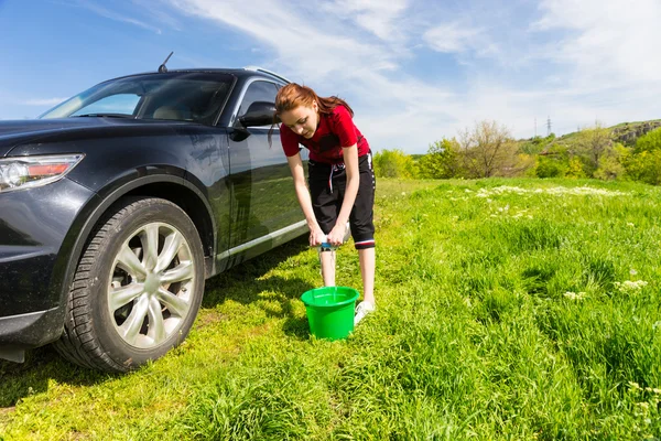 Kvinna med hink vrider ut svamp bredvid bilen — Stockfoto