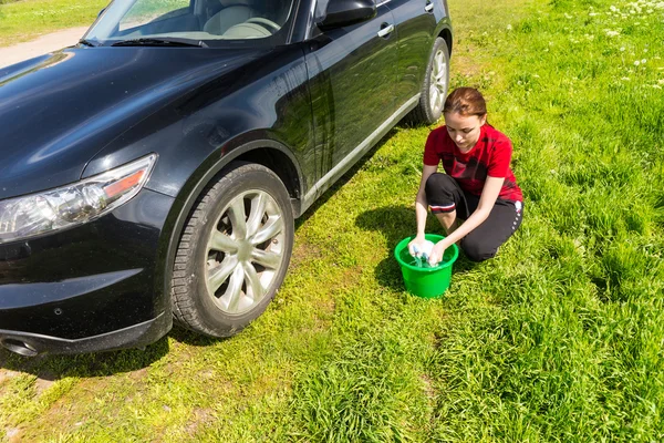 Mulher com balde arrancando esponja ao lado do carro — Fotografia de Stock