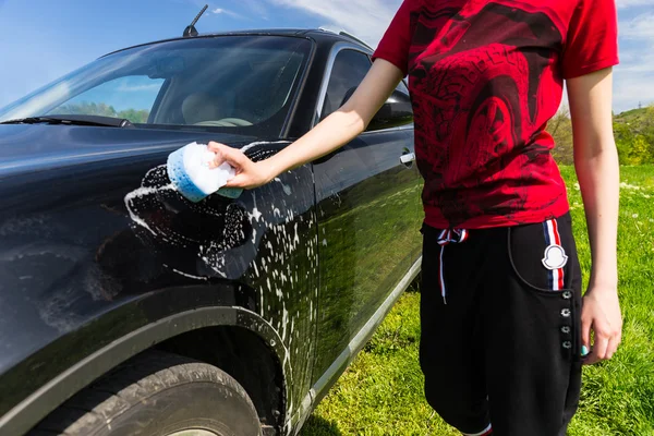 Mulher lavando carro preto no campo verde — Fotografia de Stock