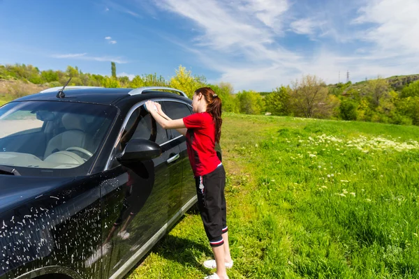 Frau wäscht schwarzes Auto im Feld mit Seifenschwamm — Stockfoto