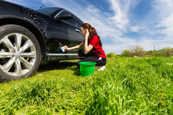 Mujer lavando coche negro con esponja en el campo verde — Foto de Stock