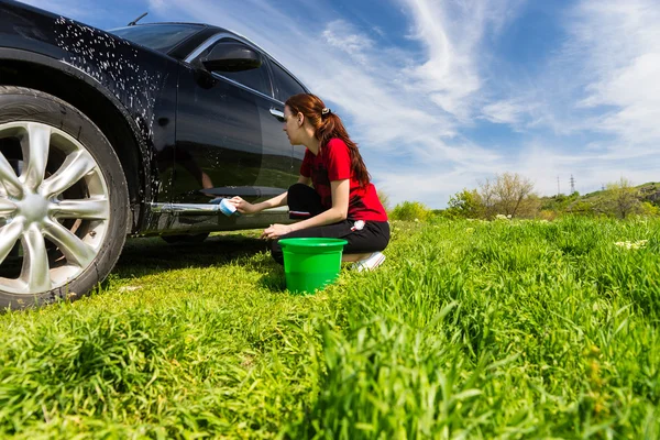 Mujer lavado coche negro en el campo con esponja jabonosa —  Fotos de Stock