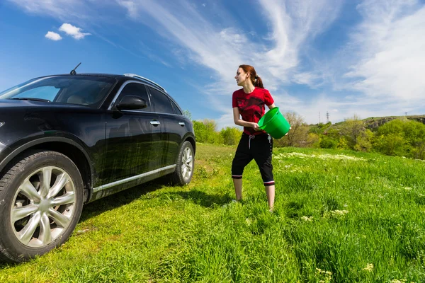 Vrouw auto met emmer Water wassen in veld — Stockfoto