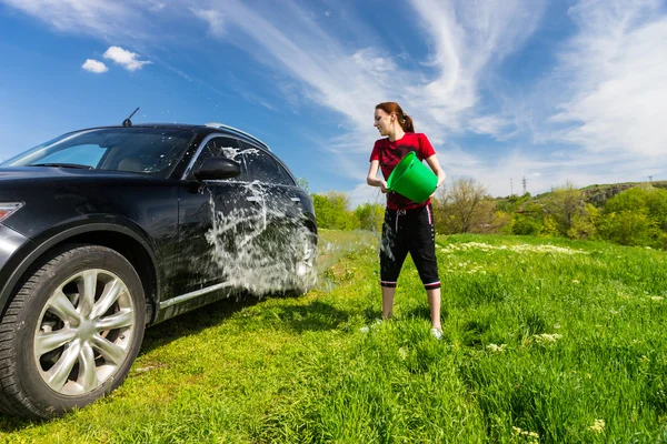 Kobieta, mycia samochodu z wiadra z wodą w dziedzinie — Zdjęcie stockowe
