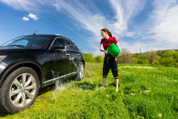 Frau wäscht Auto mit Eimer Wasser auf Feld — Stockfoto