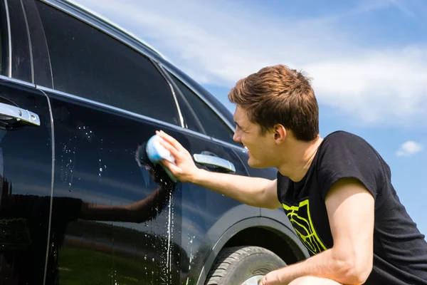 Homem que lava o carro preto com esponja ensaboada — Fotografia de Stock