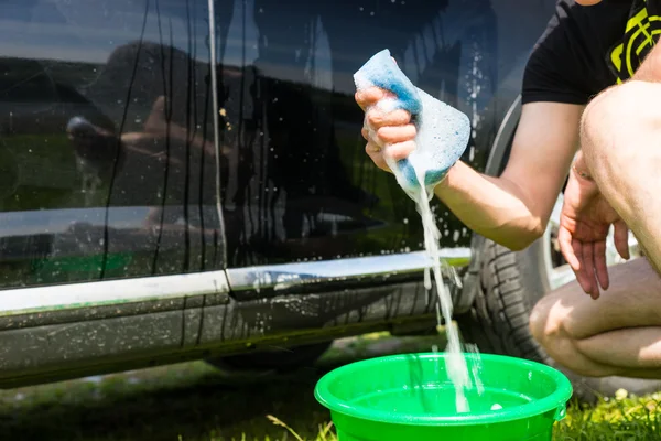 Man knijpen zeepachtige blauwe spons naast auto — Stockfoto