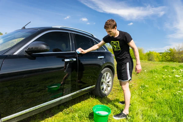 Mann wäscht Auto an sonnigem Tag auf Feld — Stockfoto